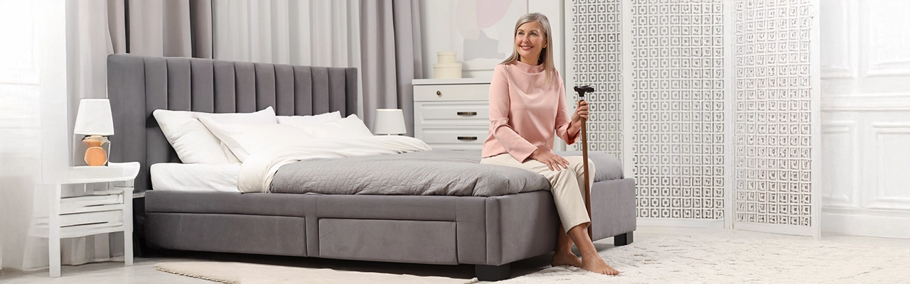 Woman sitting on bed holding cane.