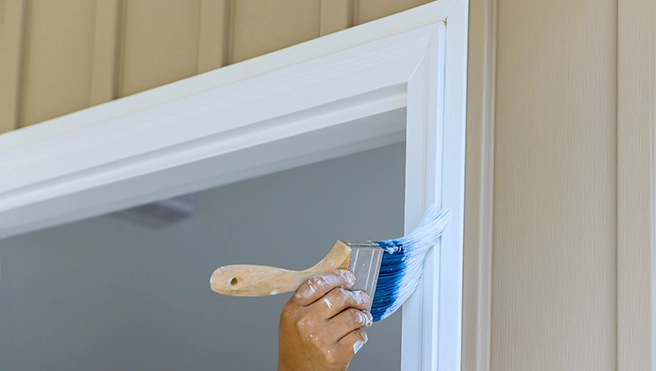 A picture of a person painting a doorframe.