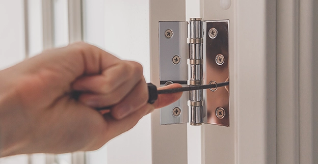 A hand securing a door hinge with a screwdriver.