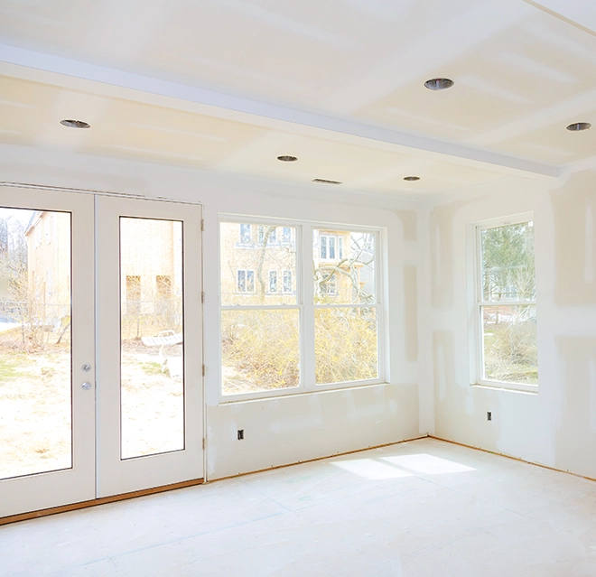 Bright, empty room with drywall and recessed lighting, featuring large double doors and windows.