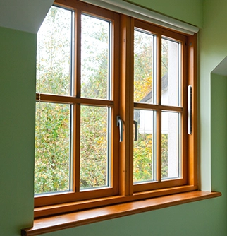 Wooden framed windows with multiple panes, showcasing a view of greenery outside, set against a light green wall.