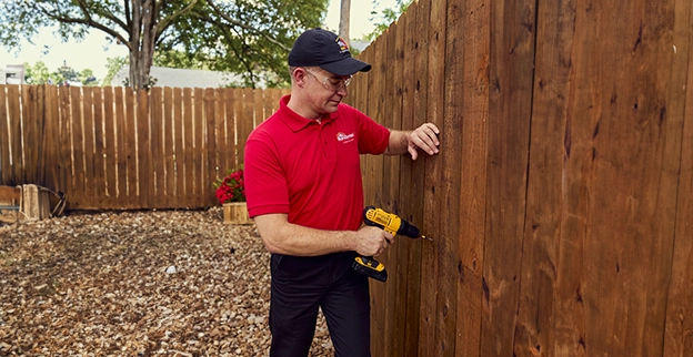 A man fastening a wooden fence with a drill.