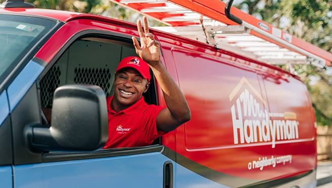 A Mr. Handyman service professional waving from a branded van.