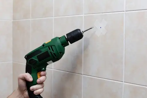 Drilling into tile with painter&rsquo;s tape to prevent cracking during towel rack installation.
