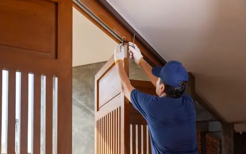 A professional handyman tightening a door hinge with a screwdriver to fix a sagging door.